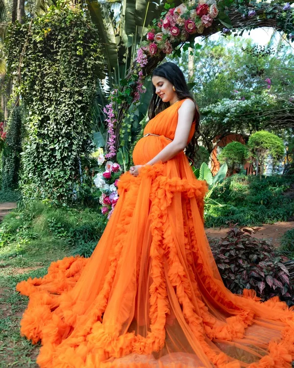 This is the kind of magical, fairy tale moment we love to create. This beautiful mom-to-be is glowing in one of our vibrant orange tulle gowns, surrounded by the lush greenery of a Bengaluru garden.