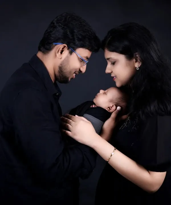 An intimate family moment captured in our classic studio style. The parents gaze lovingly at their newborn, their faces close together, creating a powerful image of connection against a simple black background.