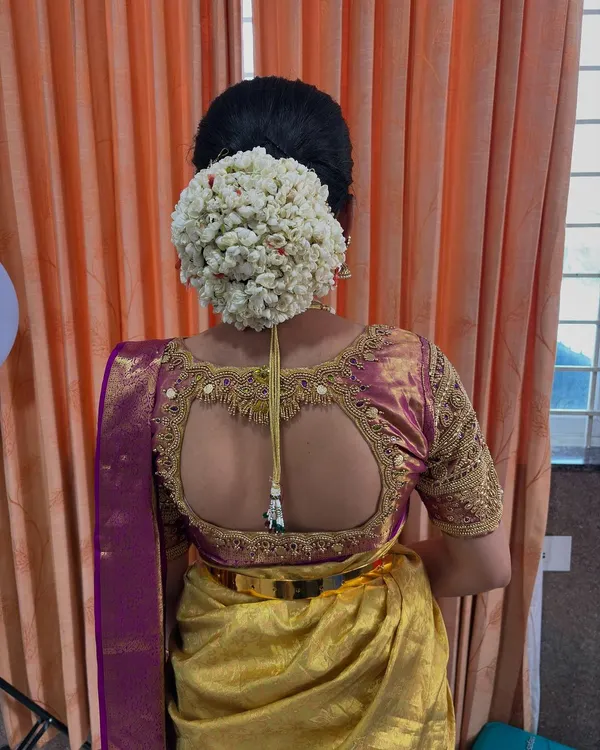 A close-up of a lush, full bun completely covered in fresh jasmine, known as malli poo. This is a classic and fragrant hairstyle that adds a touch of timeless grace to any traditional outfit.