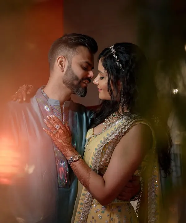 An intimate couple portrait shot through foreground elements, creating a dreamy, romantic feel. The warm lighting and close embrace make this a very powerful image.