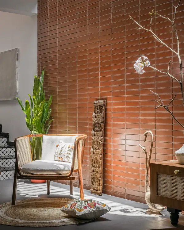 An exposed brick wall, made from local 'ittige', serves as a warm, textured backdrop for a contemporary cane armchair and traditional Indian artifacts in this cozy reading nook.