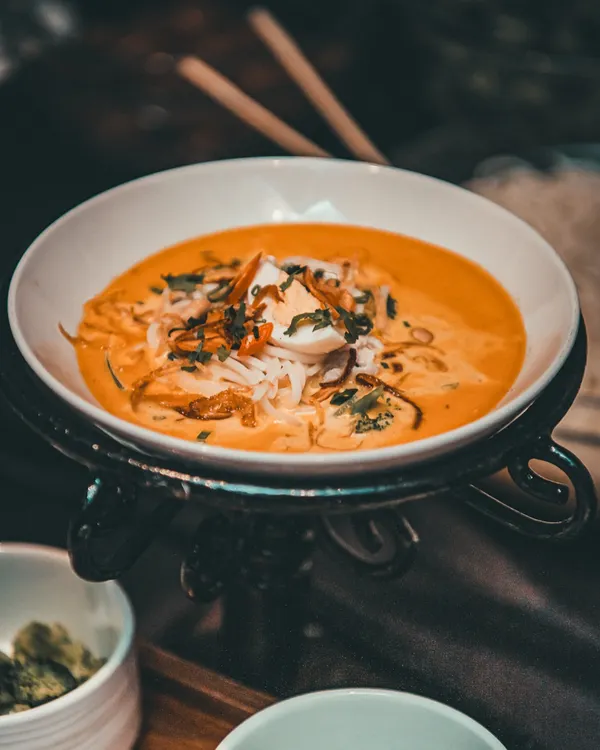 A beautifully presented bowl of Khow Suey, a Burmese noodle soup, showcasing our Pan-Asian expertise.