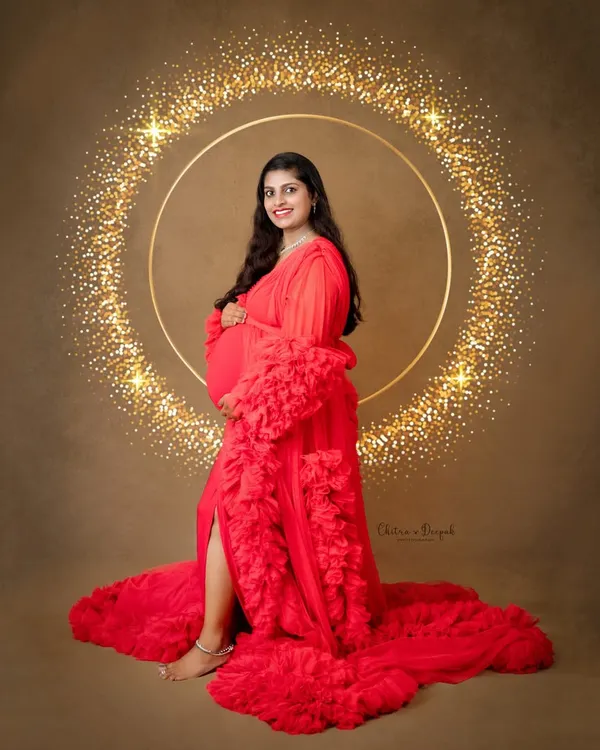 A vision in red. This mom-to-be is glowing in one of our signature ruffled gowns, set against a sparkling gold halo backdrop for a touch of high-end glamour.