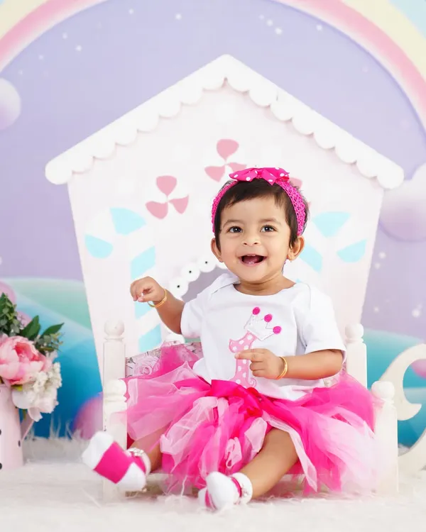 A joyful first birthday shoot! This little girl is shining in her pink tutu, sitting in front of a cute dollhouse prop with a rainbow background.