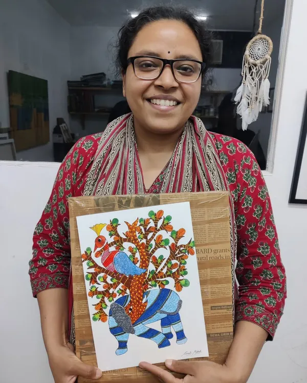 A student proudly holds her completed Gond painting of an elephant, showcasing the distinctive patterns and vibrant colors of this traditional tribal art form.