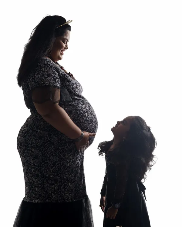 A stunning black and white silhouette of a pregnant mother and her daughter. The daughter looks up at her mother's belly with wonder, creating a powerful and emotional maternity portrait.