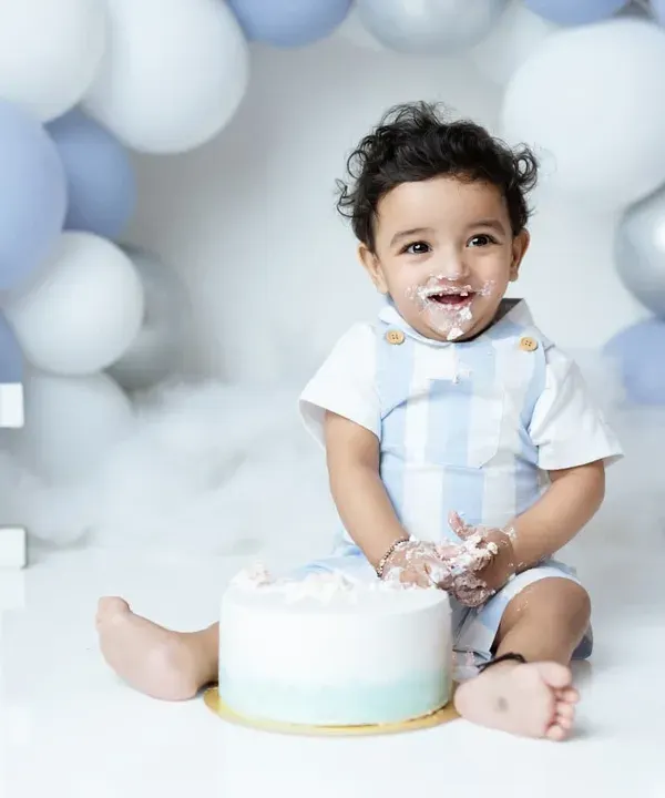 A messy and happy moment from a first birthday cakesmash. This little boy is enjoying his first taste of cake in our blue and white balloon setup.