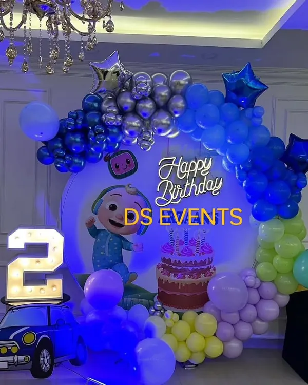 A vibrant Cocomelon birthday setup perfect for a second birthday. This decoration features a circular backdrop with the main character, a colorful balloon garland, a light-up marquee number "2", and a bright neon sign.