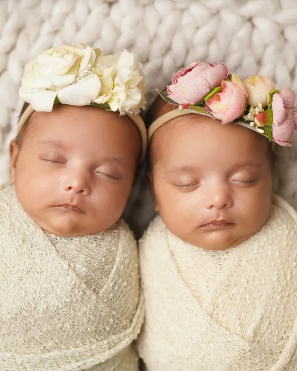 Two peas in a pod. These twin newborn girls are swaddled and sleeping side-by-side, each wearing a beautiful floral headband.
