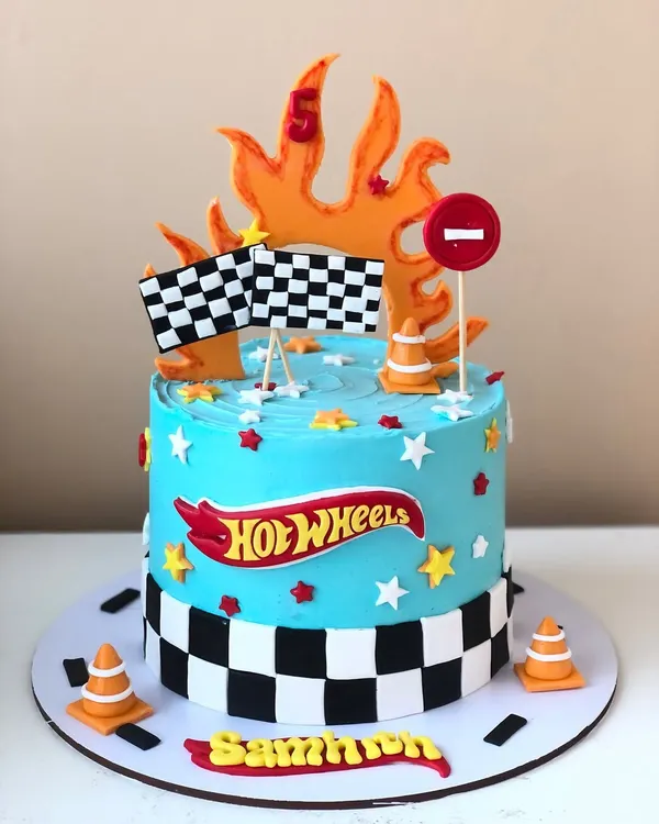 A fiery Hot Wheels cake for a fifth birthday, complete with a racetrack border, checkered flags, and traffic cones.