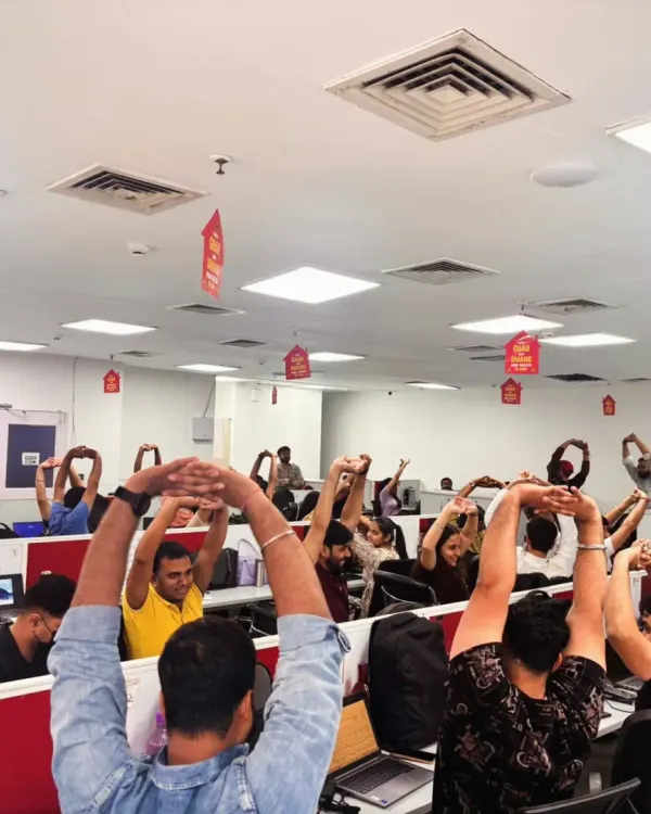 A full team engaged in a synchronized desk stretch. This simple overhead arm stretch helps to open up the shoulders and lengthen the spine, providing immediate relief from the strain of sitting at a computer.