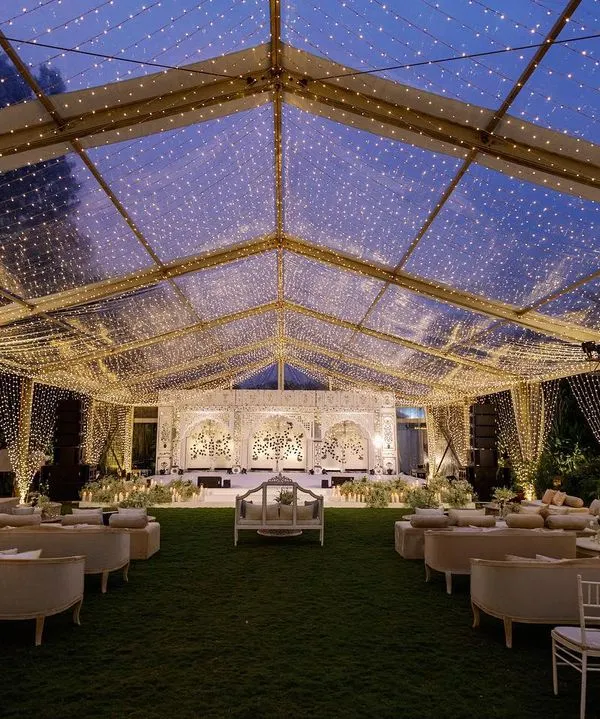 A magical sangeet night under a canopy of countless fairy lights. This custom clear-top tent allows for a celebration under the stars, while the intricate, handcrafted Thikri mirror-work backdrop adds a layer of royal Rajasthani elegance to this Bangalore event.
