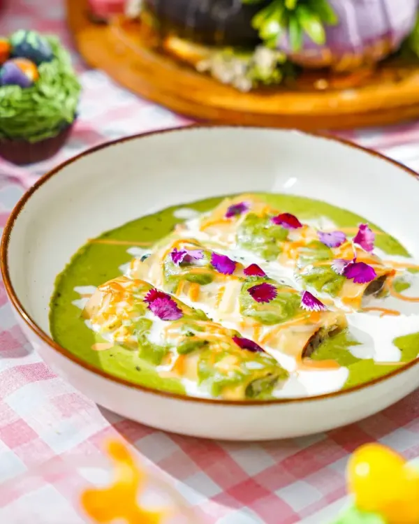 A vibrant bowl of green curry with cannelloni, garnished with edible flowers, as part of a whimsical Easter brunch. The bright, festive setting enhances the dish's appeal.