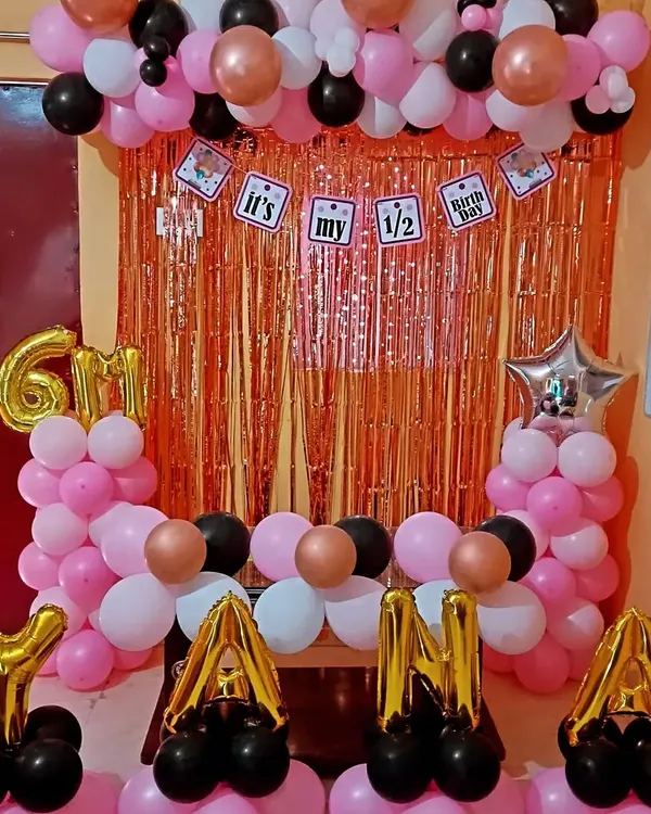 A fun half-birthday decoration for a 6-month celebration. This setup includes a rose gold tinsel backdrop, a balloon frame, and the baby's name "YANA" in foil letters.