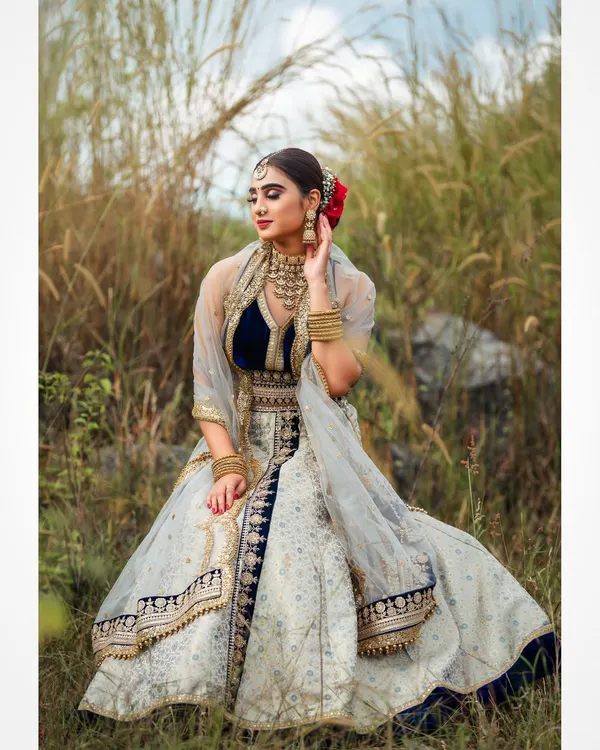 An outdoor bridal shoot capturing a serene and elegant moment. The natural setting complements the traditional lehenga, and the soft lighting highlights the delicate details of the fabric and embroidery.