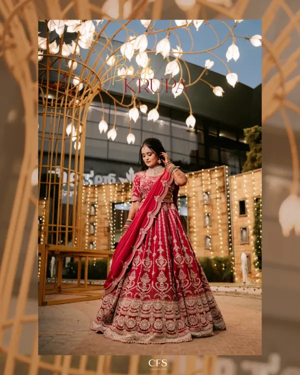 A stunning full-length portrait of the bride in her magnificent red reception lehenga. The festive lights create a magical backdrop, highlighting her elegance and the grandeur of the occasion.