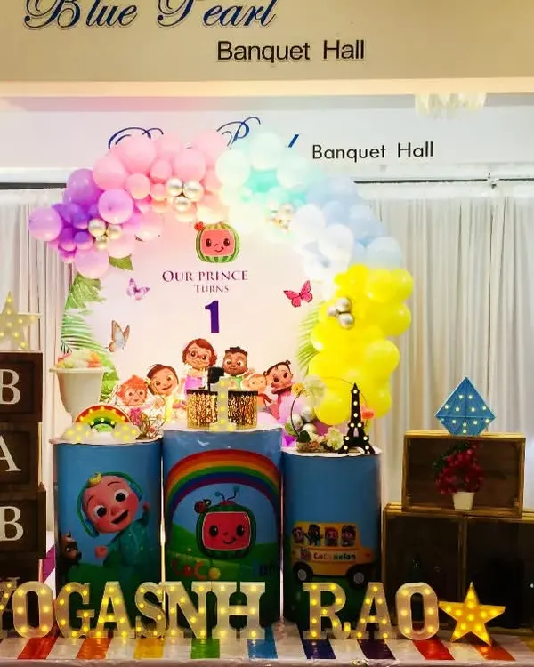 A colorful Cocomelon theme for Yogashnh Rao's first birthday. This setup features the whole Cocomelon family on the backdrop, themed pedestals, and a large JJ cutout.