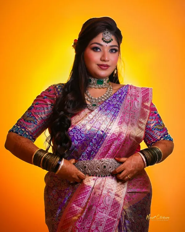 A stunning bridal portrait against a vibrant yellow backdrop. The rich colors of her saree and jewelry create a powerful and beautiful image.