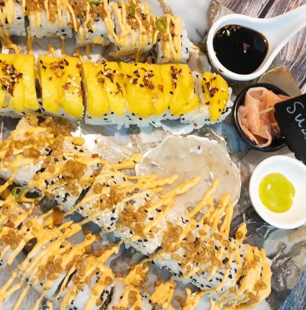 An overhead view of our assorted sushi platter. We offer a wide variety of rolls, including tempura, classic maki, and uramaki, all drizzled with delicious sauces and served with wasabi and soy.