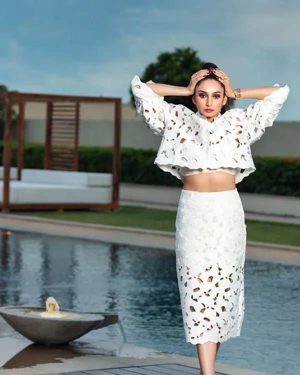An editorial shot of actress Ragini Dwivedi for a magazine cover. The poolside location and the unique white cutout dress create a majestic and high-fashion look.
