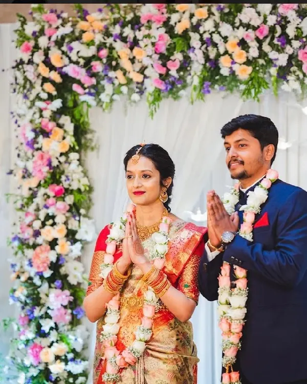 A happy couple during their engagement ceremony, framed by a beautiful arch of pastel-colored flowers.