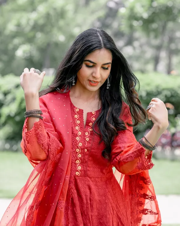 A candid moment from a pre-wedding shoot. The bride-to-be is in a beautiful red dress, captured in a natural, unposed moment in a lovely garden setting.