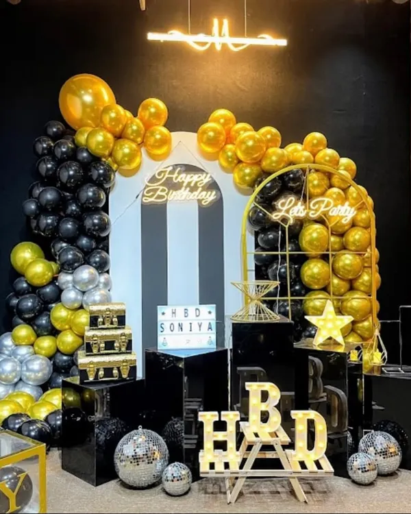A stunning black, gold, and silver theme with multiple backdrops, pedestals, and a "Let's Party" sign, creating a luxurious feel.