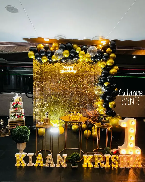 For a first birthday that truly shines, I created this glamorous black and gold theme. The setup features a full gold sequin backdrop for that sparkling effect, a custom balloon arch, and personalized light-up marquee letters for the name 'Kiaan Krish' and the number '1'.
