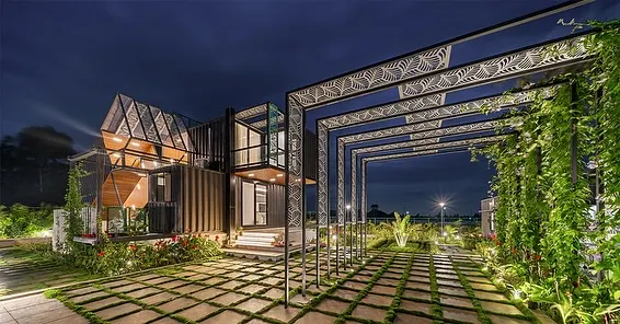 The QBINN TUSKER container home illuminated at night, with a vine-covered pergola creating a dramatic, glowing entryway. This shot captures the project's innovative use of industrial materials and landscape integration.