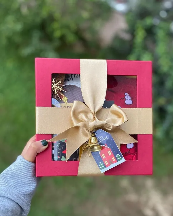 The perfect Christmas gift, all wrapped up and ready to go. This red window box is tied with a gold ribbon and a jingle bell, offering a festive preview of the holiday-themed goodies waiting inside.