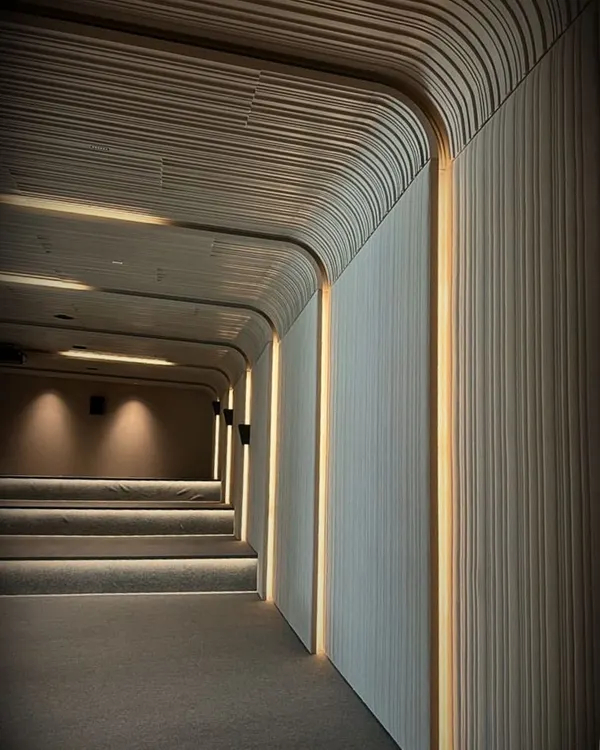The entrance to a home theater, where curved, fluted walls and integrated strip lighting create a gentle, flowing path into the immersive space. The design focuses on creating a tranquil and refined cinematic environment.