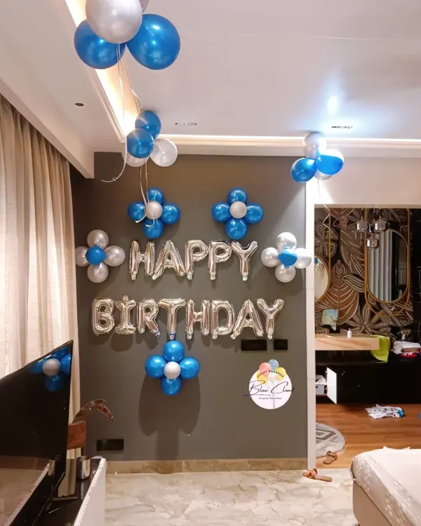 A classic 'Happy Birthday' wall decoration with silver foil letters, blue and silver balloon flowers, and ceiling bunches.