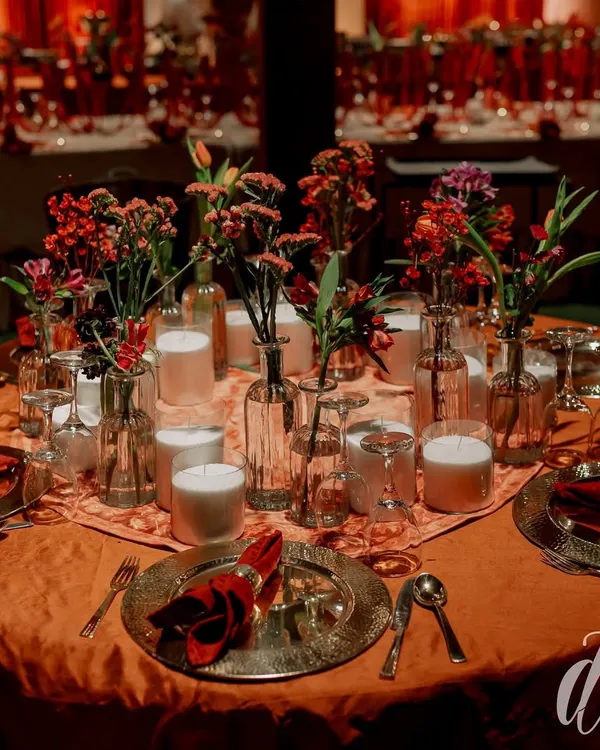 The tables were set with deep orange linens, hammered metal charger plates, and rich red napkins. Centerpieces of red flowers in clear glass vases, surrounded by candles, created an intimate and warm dining setting.