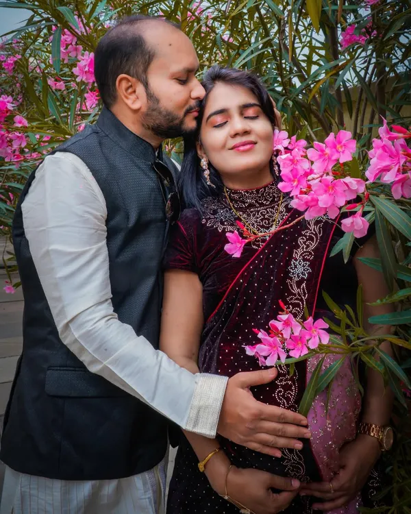 An intimate moment captured amidst blooming flowers. The partner's gentle kiss and their hands cradling the baby bump create a portrait filled with warmth and affection.