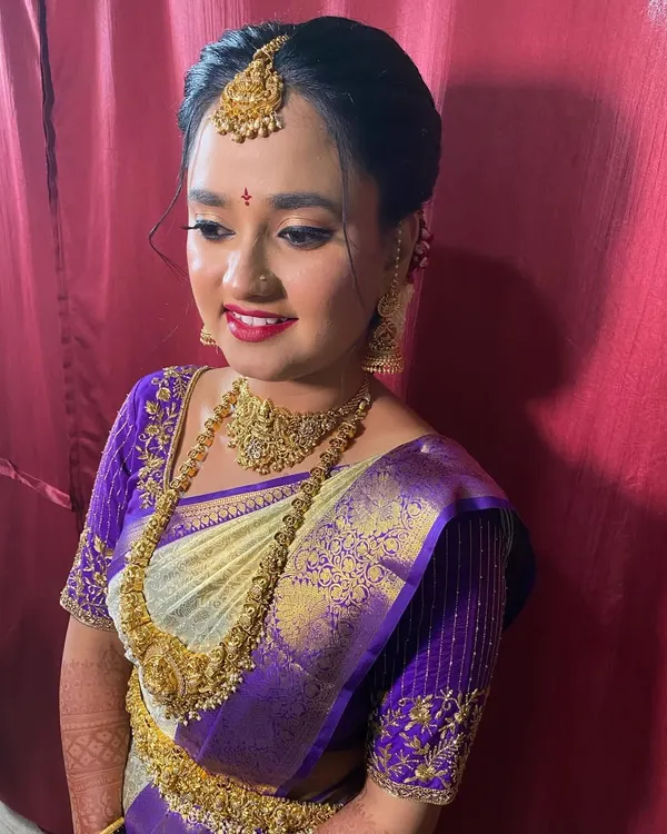 A classic bridal updo, neatly tied and puffed at the crown to support the maang tikka. This is a timeless look for a muhurtham ceremony.