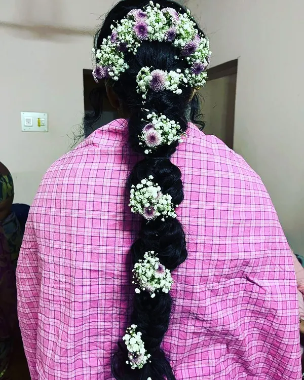 A classic South Indian bridal hairstyle featuring a thick braid adorned with fresh baby's breath and purple flowers. This style is timeless and photographs beautifully.