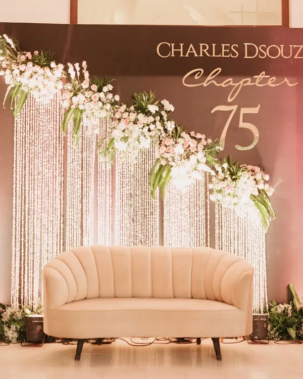 For a 75th birthday, elegance is key. We designed this sophisticated photo backdrop featuring a classic scalloped sofa, a personalized "Chapter 75" sign, and a cascade of crystals and white flowers.