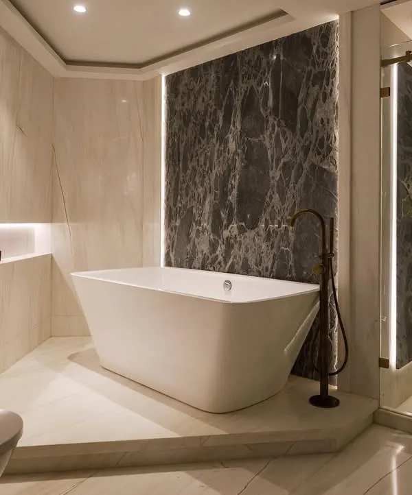 A master bathroom from our 'Urban Tranquility' project. The freestanding tub is the star, set against a dramatic dark marble accent wall. Warm, indirect lighting and light marble on the surrounding walls create a chic, spa-like atmosphere.