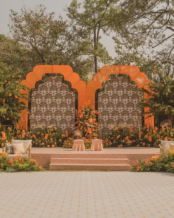 The main stage for our 'Orange Orchard' Haldi ceremony, featuring a backdrop of custom-printed fabric framed by vibrant orange arches and surrounded by orange trees.