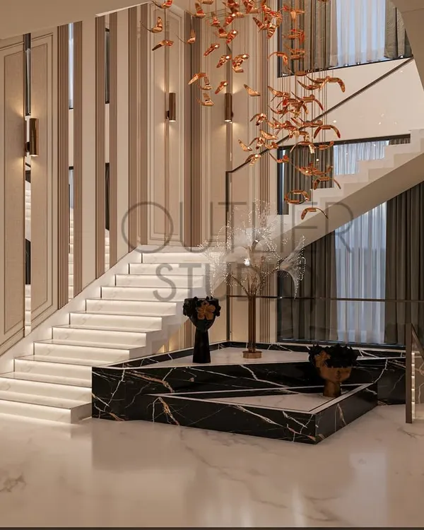 The base of this staircase is a sculptural platform made of black marble, serving as both a functional step and an art installation. A cascading metallic light fixture hangs above, drawing the eye upward.