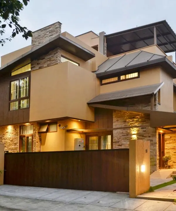 This modern rustic home, known as the 'Mountain Abode', captures the feeling of a mountainside retreat. The exterior lighting design highlights the texture of the stacked stone and the clean lines of the metal-clad roof against the evening sky.
