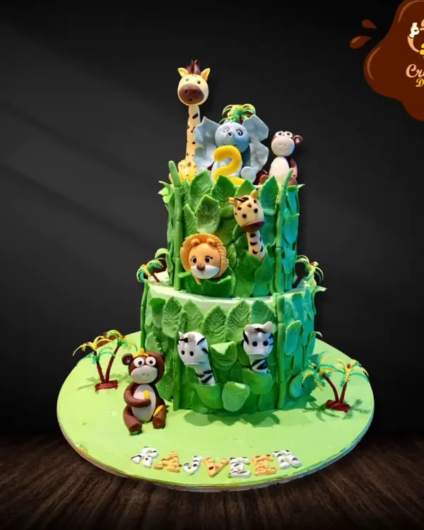 This two-tier jungle cake is covered in lush green fondant leaves. It features adorable animals like a giraffe, elephant, lion, and monkeys peeking out, creating a fun safari adventure for a second birthday.