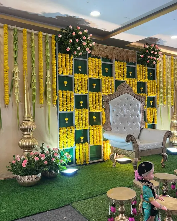 A beautiful stage setup for a traditional ceremony, featuring a backdrop of marigolds, hanging flower garlands, and an ornate white chair for the guest of honor.