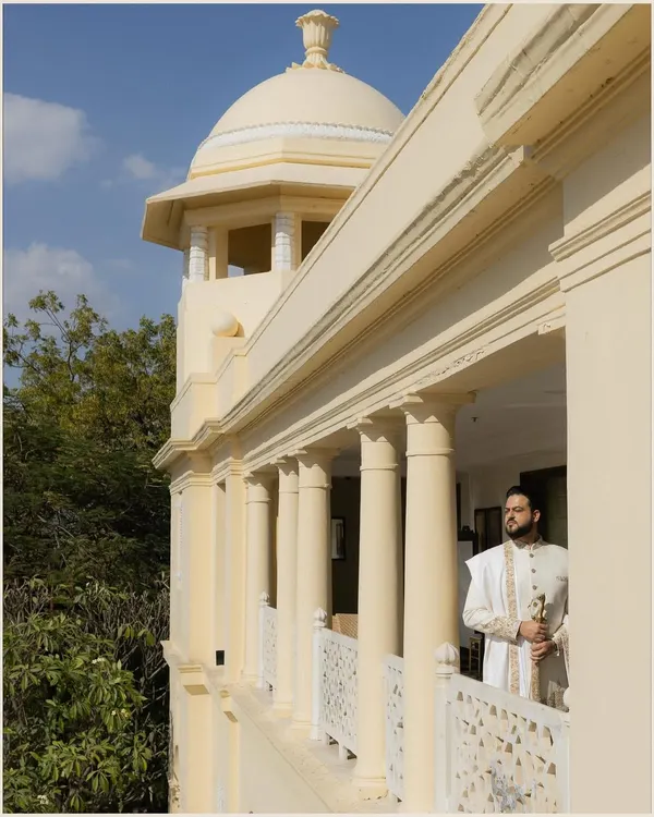 A regal portrait of the groom standing on a palace balcony, looking out thoughtfully. The architecture and natural light create a majestic and timeless feel.