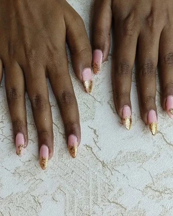 An elegant set of gel nail extensions. We created this look with a soft pink base and added a touch of glamour with gold glitter tips and subtle stone work, perfect for a special occasion.