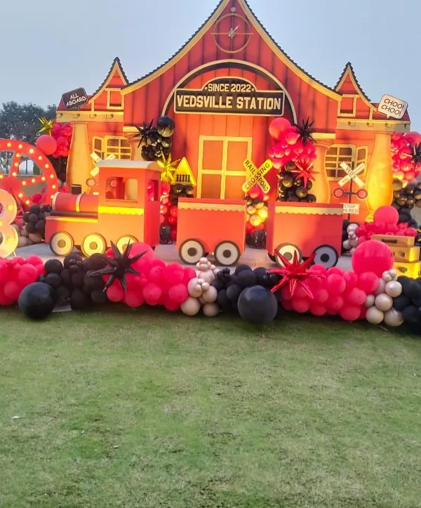We specialize in bringing imaginative worlds to life, like this custom vintage train station created for a truly unique third birthday. This large-scale outdoor setup features a detailed station house, a 3D train, and themed props, all tied together with a dramatic red and black balloon garland.