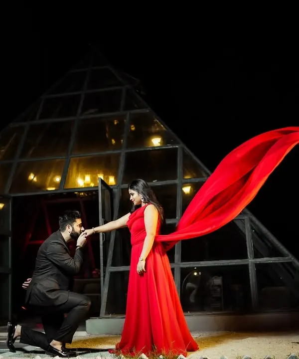 A dramatic pre-wedding photo at night. The groom's proposal pose, the bride's flowing red dress, and the unique pyramid location create a truly cinematic and memorable shot.