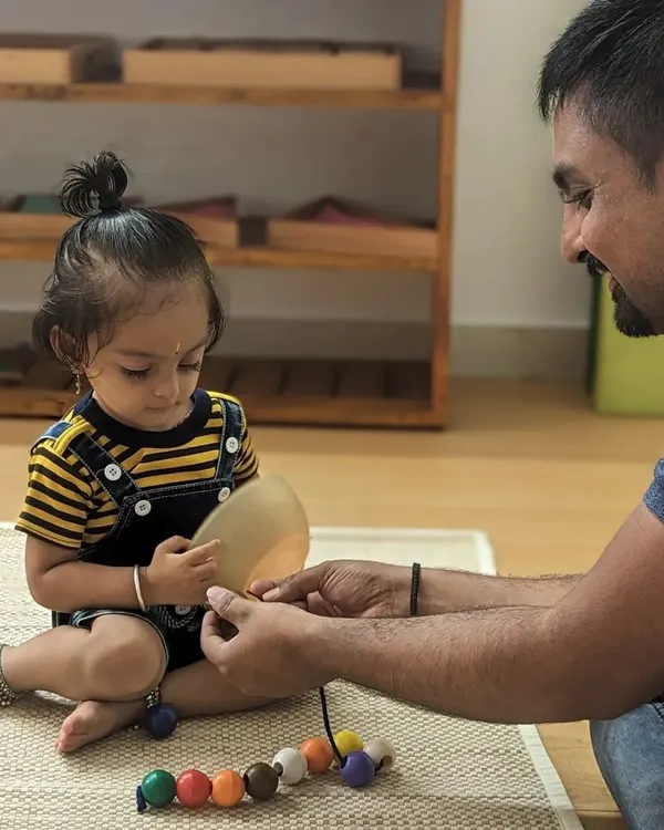 A father guides his daughter in a beading activity, a simple joy that helps develop fine motor skills and concentration. These one-on-one moments are precious parts of the learning process.