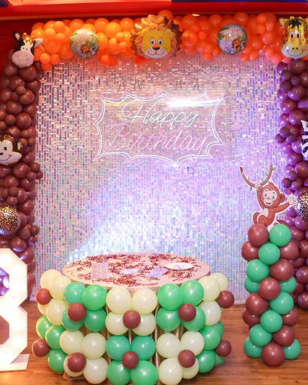 A complete jungle safari theme setup for a 3rd birthday. This includes a custom cake table made of balloons, a large light-up number, and a sparkling backdrop with animal character balloons.
