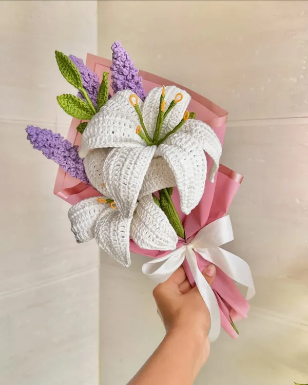 A stunning custom bouquet featuring handcrafted white crochet lilies and delicate purple lavender stems. The combination of colors and textures, wrapped in pink paper with a white satin bow, makes for an elegant and timeless gift.